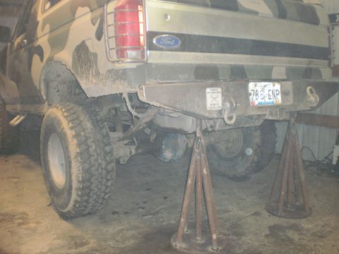 1995 Ford Bronco - Rear view of a camouflaged Ford Bronco, supported by jack stands, with visible suspension components and a license plate.