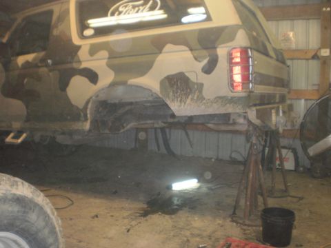 1995 Ford Bronco - This Ford Bronco, painted in camouflage, is elevated on jack stands with its rear axle removed, suggesting mechanical work.