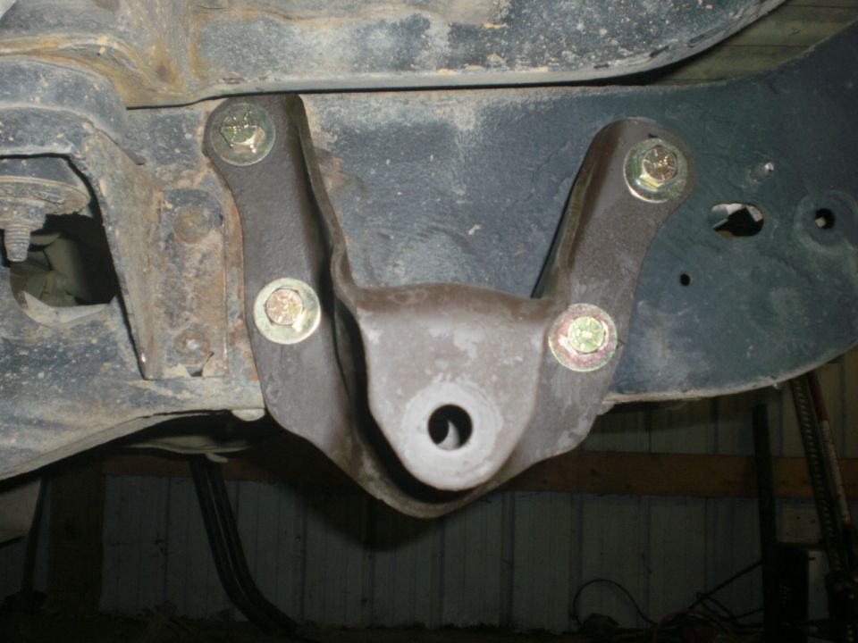 Close-up of a rusty metal suspension bracket with four bolts attached to a vehicle frame