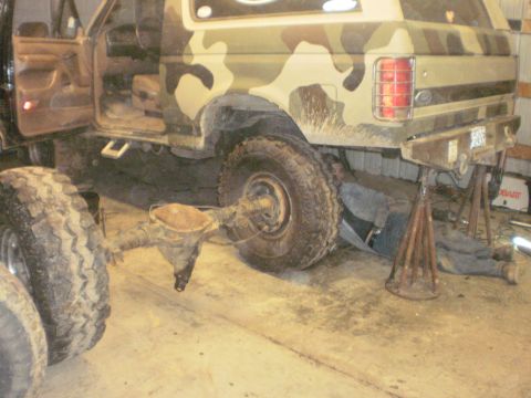 1995 Ford Bronco - A 1995 Ford Bronco, painted in camouflage, is shown with its rear axle removed as a person works underneath it.