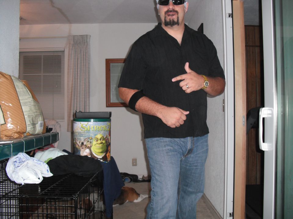 Man in black shirt and jeans pointing, with a Shrek trash can