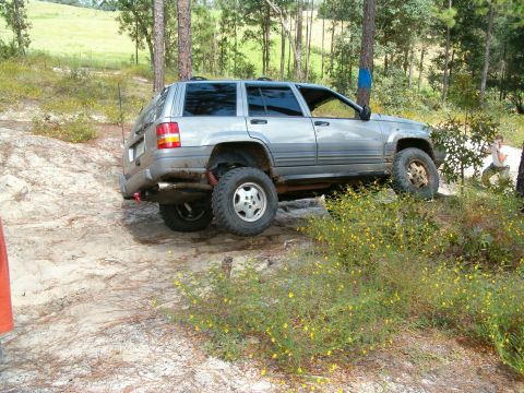 1991 Ford Bronco - Silver Jeep Grand Cherokee navigates a challenging off-road trail with yellow wildflowers in the foreground.