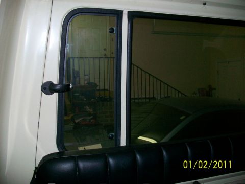 1986 Jeep Wagoneer - Interior view of a white Jeep showing a rear quarter panel window with a reflection of a doorway and another vehicle.