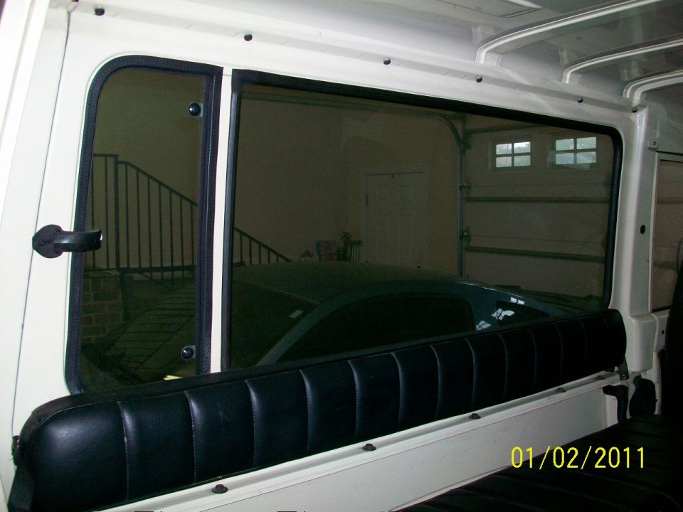 Bare white SUV interior with black vinyl rear bench and sliding side window looking into a garage