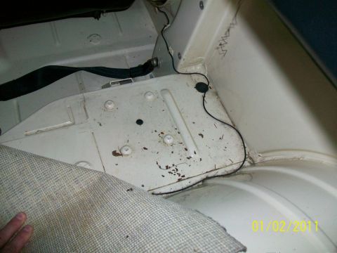 1986 Jeep Wagoneer - The interior floor of a vehicle shows signs of wear and tear, with rust spots and exposed wiring visible.