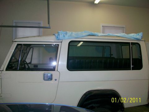 1986 Jeep Wagoneer - This white Jeep SUV is seen from the side, with a blue tarp covering the roof area.
