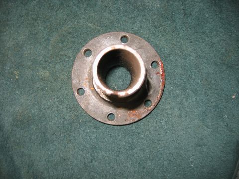 1992 Ford Bronco - A flanged pipe fitting with six bolt holes is shown against a dark green textured background. The part shows signs of rust.