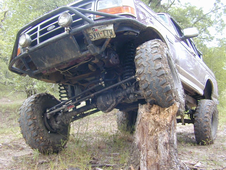 Lifted Ford Bronco on a tree stump, front wheel lifted, showing axle and mud tires
