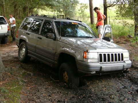 1991 Ford Bronco - A silver Jeep Grand Cherokee is stuck in the mud with another vehicle nearby. The scene appears to be off-road.