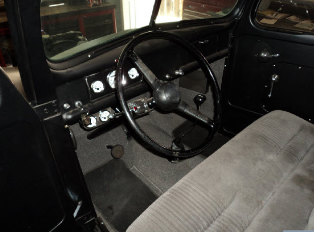 Vintage pickup cab interior with black steering wheel, painted dash and gray bench seat
