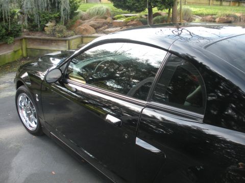 2003 Ford Mustang - A black coupe with shiny chrome wheels is parked outdoors on a paved surface.