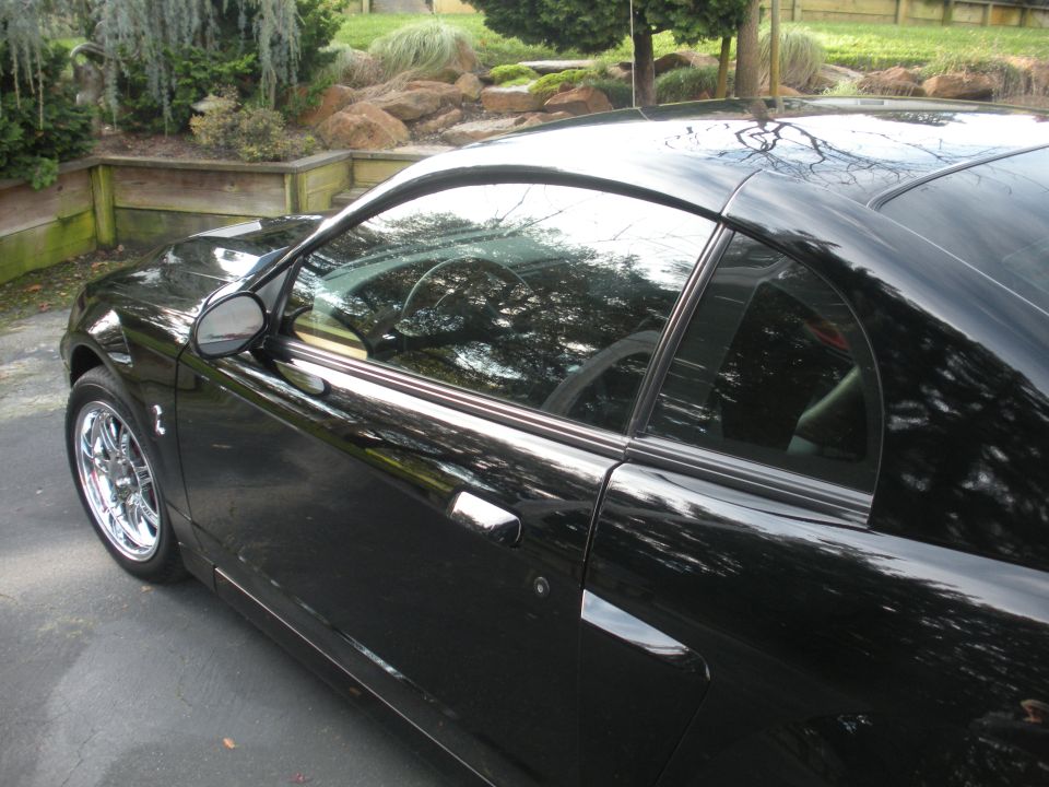 Black coupe with chrome wheels, side view. Interior visible through windows