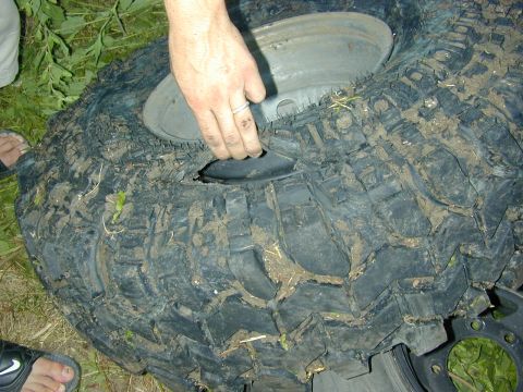 1996 Ford Bronco - A damaged tire lies on the ground, with a hand inspecting the large hole.