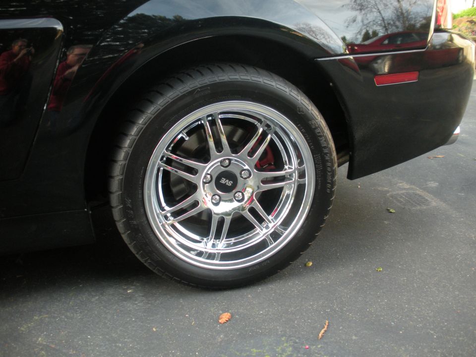 Black car rear quarter panel and chrome wheel with red brake caliper visible