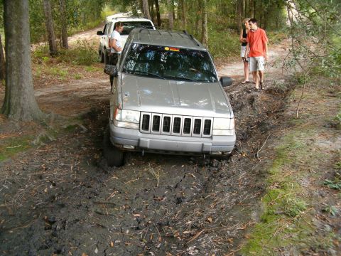 1991 Ford Bronco - A silver Jeep Grand Cherokee navigates a muddy trail, with a white SUV following behind.