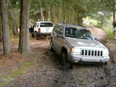 1991 Ford Bronco - Two Jeep Grand Cherokees are stuck in the mud on a dirt path.