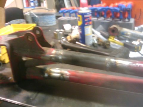 1995 Ford Bronco - Metal components with fresh welds sit on a cluttered workbench, suggesting ongoing repair or fabrication.