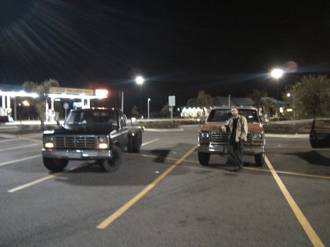 1984 Ford Bronco II - Two Ford trucks, one black dually and one orange, parked in a lot at night with a man by the orange truck.