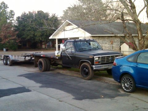 1984 Ford Bronco II - A black Ford F-350 flatbed truck with dual rear wheels tows a trailer while parked on a street.