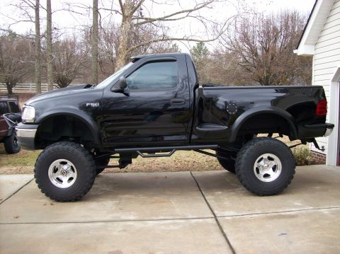 2000 Ford F-150 - A lifted black Ford F-150 pickup truck is parked on a concrete driveway.