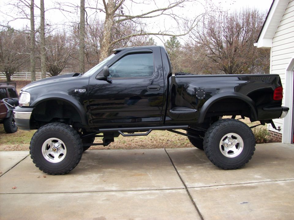 Lifted black Ford F-150 pickup truck, side view. Has F-150 badge on fender