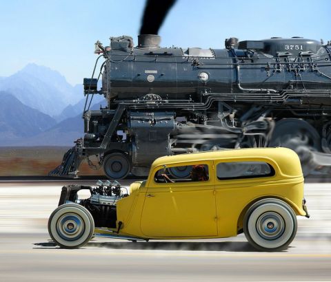1991 Ford LTD Crown Victoria - Composite action shot of a yellow chopped 1930s Ford sedan hot rod running alongside a black steam locomotive numbered 3751 with desert mou…