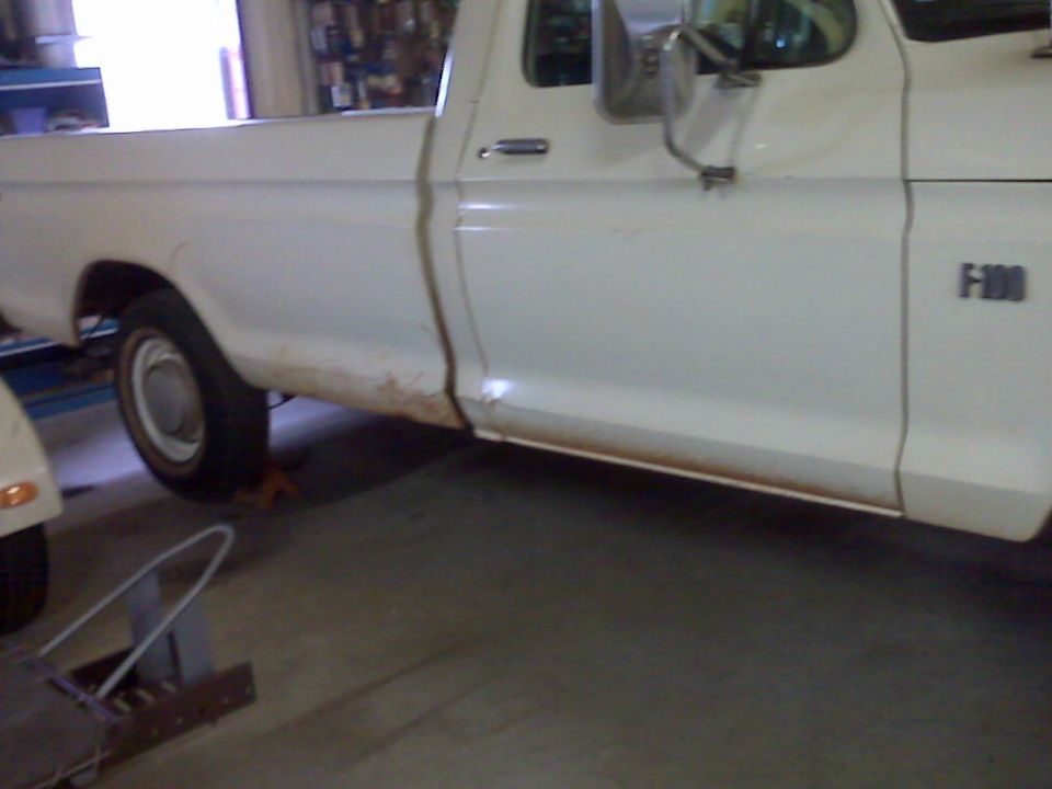Side view of a white 1973 Ford F-100 pickup truck with rust on the lower body
