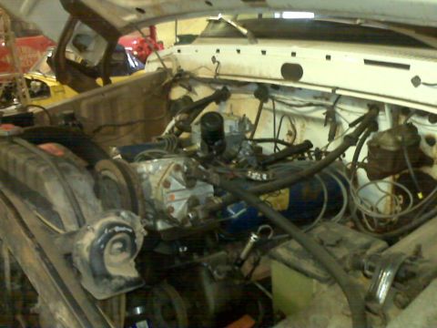 1973 Ford F-100 - The engine bay of a white truck is shown, various mechanical parts and wiring harnesses.