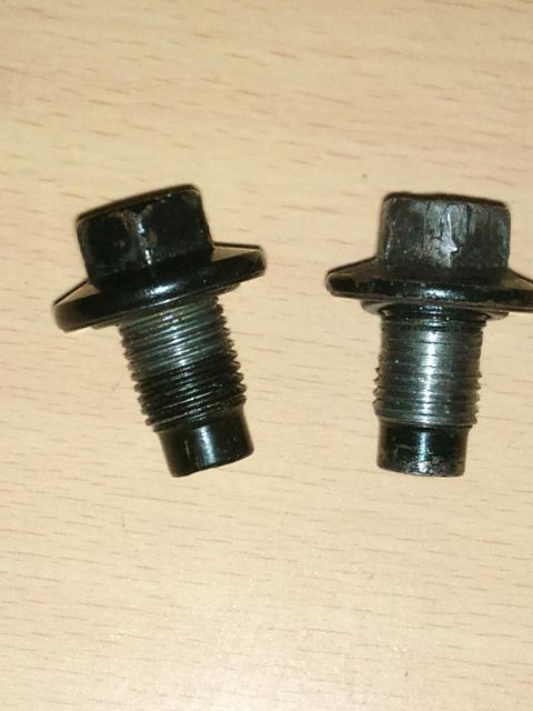 1998 Ford Crown Victoria - Two black oil pan drain plugs are shown on a wooden surface.