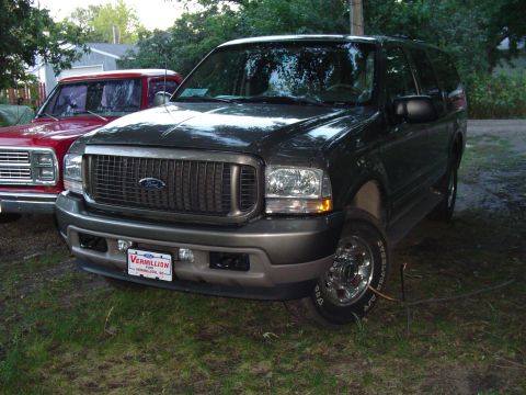 1986 Ford Bronco - Ford Excursion SUV parked next to a red Dodge Ram pickup truck in a grassy area.