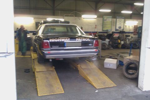1991 Ford LTD Crown Victoria - Rear view of a dark Ford Crown Victoria police sedan with white "HIGHWAY PATROL" lettering across the trunk lid, sitting on yellow drive-on…