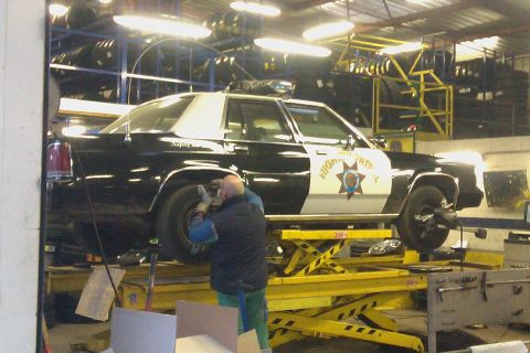 1991 Ford LTD Crown Victoria - A black-and-white Ford LTD Crown Victoria police car lettered 'HIGHWAY PATROL' with a gold star door decal sits raised on a yellow scissor…