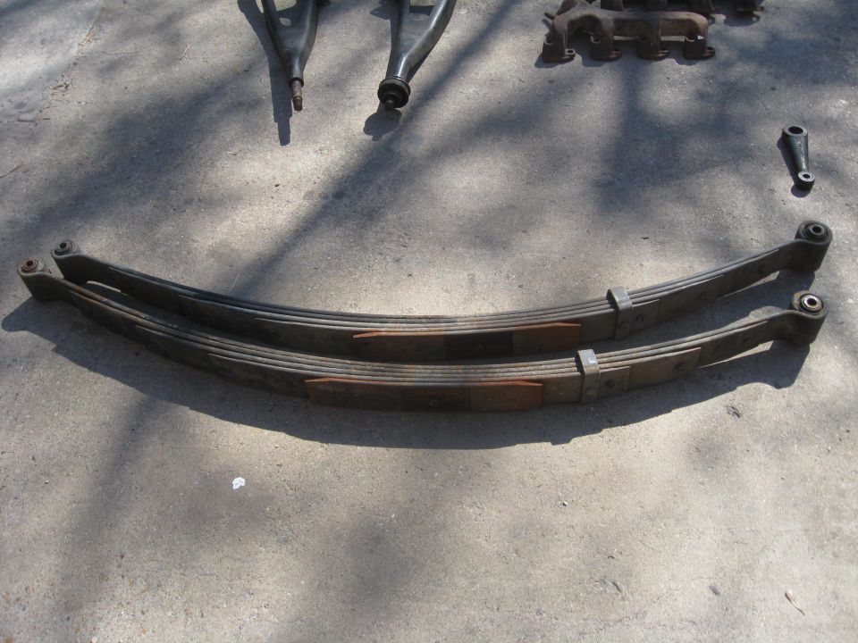 two curved leaf springs and several suspension components laid out on concrete