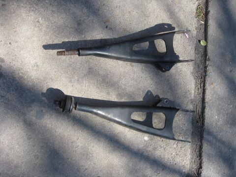 1994 Ford Bronco - Two automotive control arms are shown lying on a concrete surface, casting shadows.