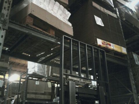 1989 Ford Bronco - A forklift is positioned in a warehouse aisle, surrounded by tall shelving units filled with various goods.