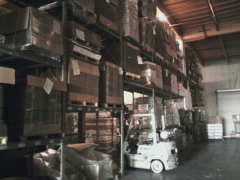 1989 Ford Bronco - A forklift sits in a warehouse aisle surrounded by tall shelves filled with boxes.