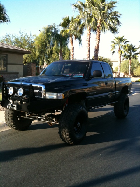 1966 Ford Bronco - This lifted black Dodge Ram pickup truck is parked on a residential street under a clear blue sky.