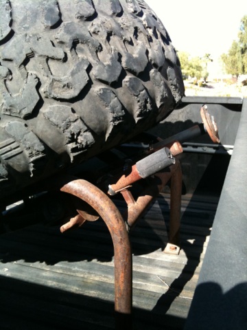 1966 Ford Bronco - A large spare tire is secured with rusty metal brackets in the bed of a pickup truck.