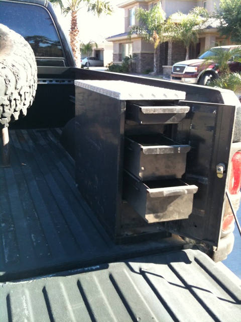 1966 Ford Bronco - A view of a truck bed a black toolbox and a spare tire, with another vehicle parked in the background.