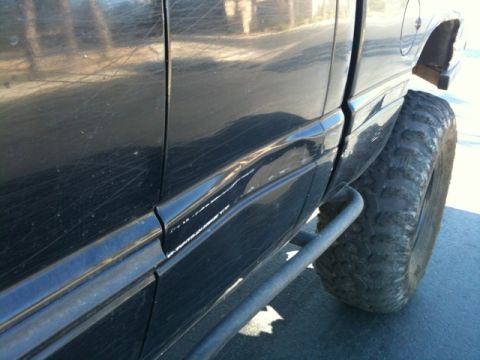 1966 Ford Bronco - Side view of a black pickup truck large off-road tires and metal side steps, showing significant body damage.