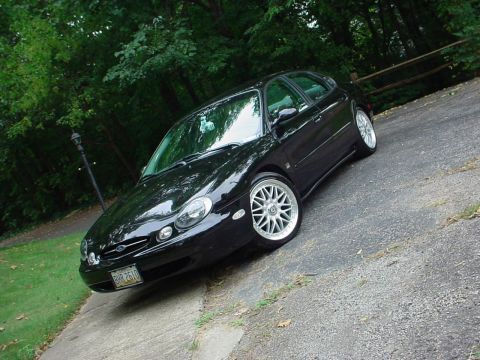 1999 Ford Taurus - This black 1999 Ford Taurus hatchback is shown from a three-quarter front angle, aftermarket wheels and a lowered stance.