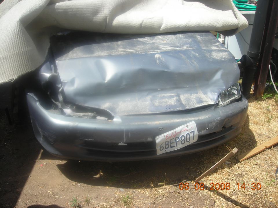 Front of a heavily damaged car, covered partially by a tarp. California license plate 6BEP807 is visible