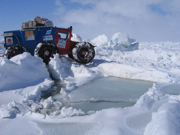 Blue and red expedition vehicle on huge tires crossing snowy ice terrain