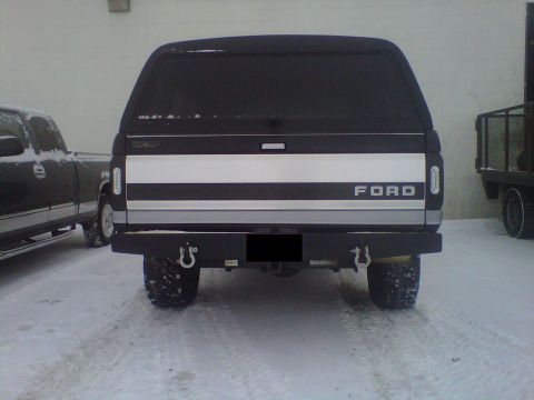 1994 Ford F-150 - A Ford pickup truck with a camper shell is parked in the snow, showing its rear end and a custom bumper.