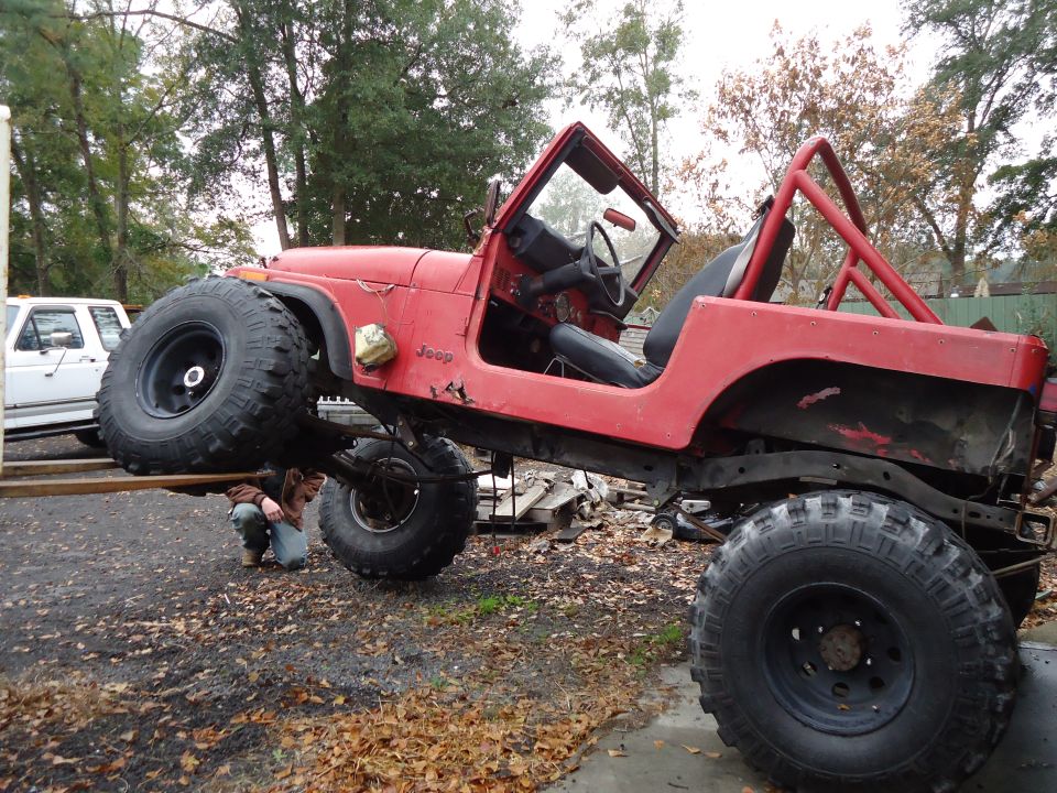 Red 1985 Jeep CJ7 lifted with large tires, being worked on