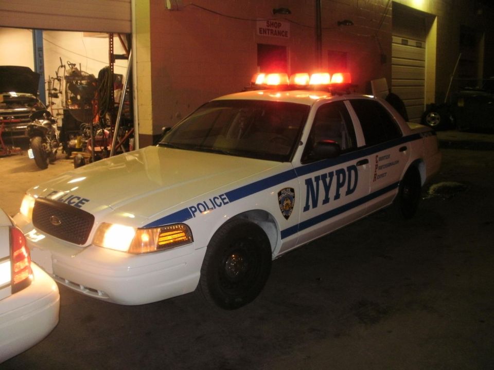 White 2002 Ford Crown Victoria police car with NYPD markings and emergency lights on