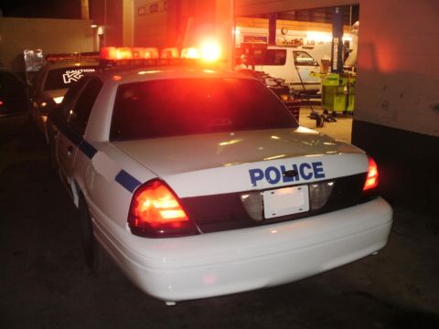 2002 Ford Crown Victoria - A police car with its emergency lights activated is parked inside a garage.