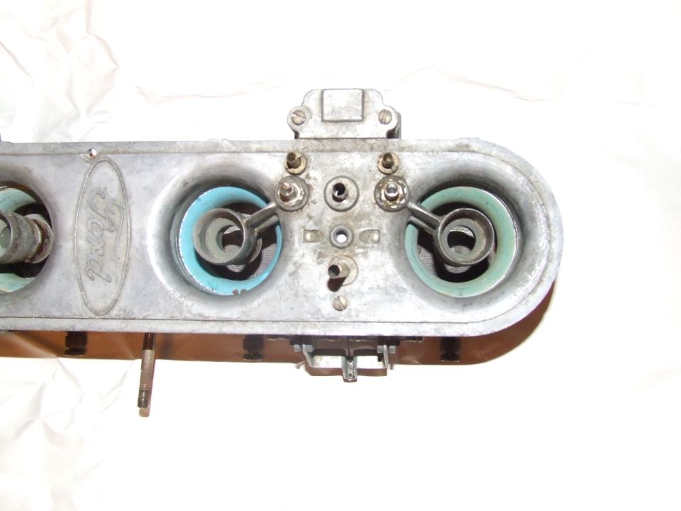 Ford carburetor with two blue-green gaskets and visible Ford oval logo