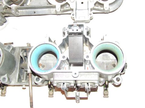 1973 Ford Mustang - Close-up of a carburetor part, showing intricate mechanical components and intake openings.