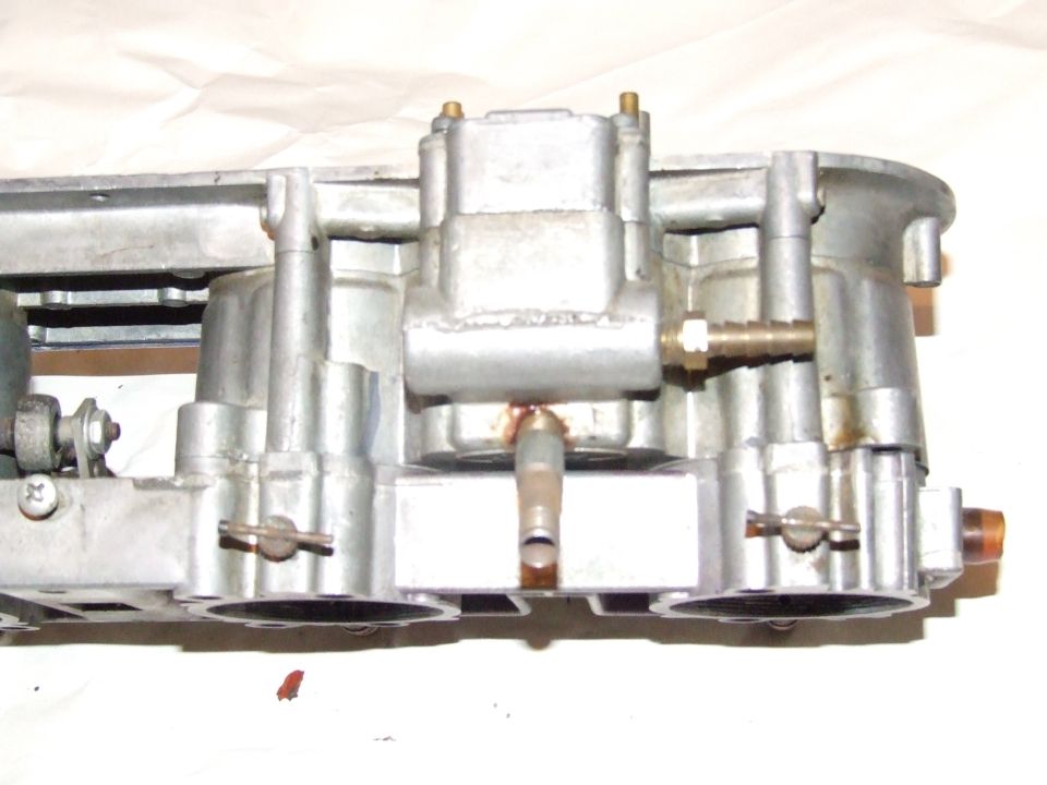 Close-up of a metal carburetor assembly with fuel lines attached
